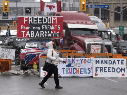 A woman crosses the street in front of vehicles parked as part of the trucker protest, Tue