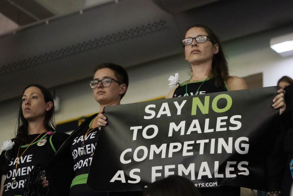 Protesters, one holding a sign, stand as Pennsylvania transgender athlete Lia Thomas competes in the women's 200 freestyle final at the NCAA swimming and diving championships Friday, March 18, 2022, at Georgia Tech in Atlanta. Thomas finished tied for fifth place. (AP Photo/John Bazemore)