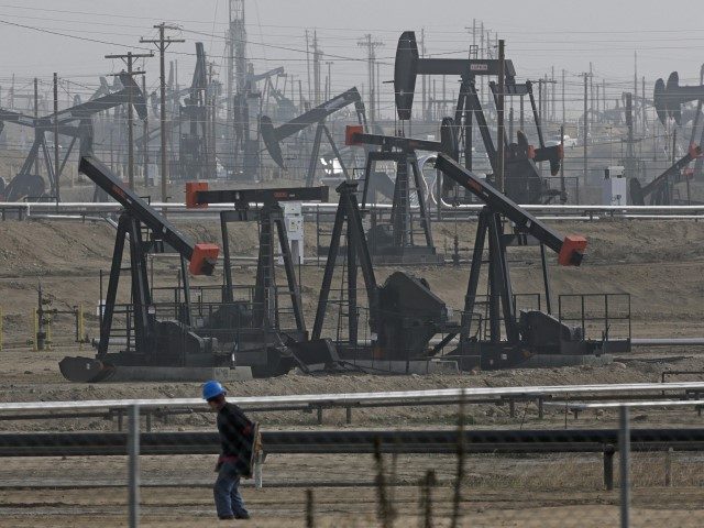 In this Jan. 16, 2015, file photo, a person walks past pump jacks operating at the Kern Ri