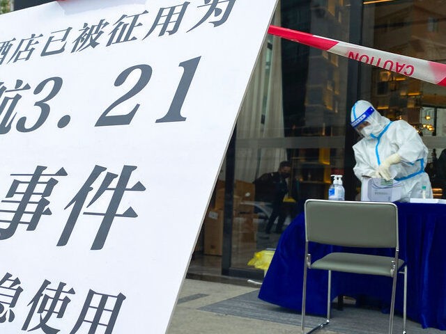 A worker wearing a protective suit prepares to assist people outside a hotel displaying a