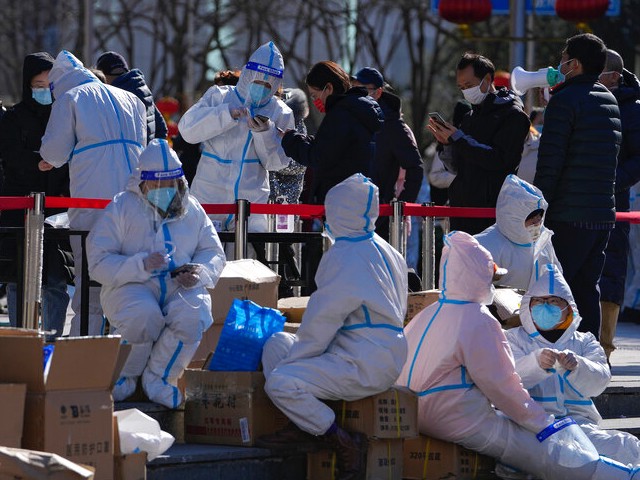 Workers in protective suits take a rest as people line up to register during a mass COVID-19 test outside a shopping mall in Beijing, Tuesday, Feb. 22, 2022. (AP Photo/Andy Wong)