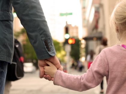 Father holding daughter’s hand on city street