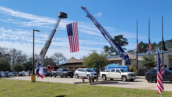 Ladder Trucks from Livingston and Montgomery County Fire Departments hoist the American flag in honor of Deputy Neil Adams. (Bob Price/Breitbart Texas)