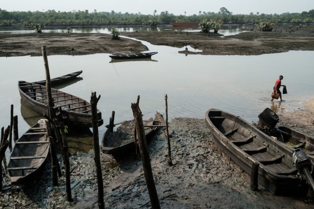 A fisherman walks by the oil smeared fishboats on oily mud in the river during low tide at Ogoniland's village of K-Dere, near Bodo, which is part of the Niger Delta region, on February 20, 2019. - Decades of oil spills has left the Ogoniland region in southern Nigeria an environmental disaster zone -- but now hopes are high of a rebirth of farming, fishing and clean water. (Photo by Yasuyoshi CHIBA / AFP)        (Photo credit should read YASUYOSHI CHIBA/AFP via Getty Images)