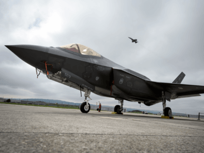 A Lockheed Martin F-35 Lightning II fighter jet is parked on the tarmac at the Payerne Air Base as a Boeing McDonnell Douglas F/A-18 Hornet takes off in the background, during flight and ground tests, as Switzerland is looking for a new fighter jet to replace its aging fleet, on …