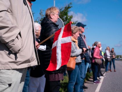 A man holds a Danish flag as he stands with other people on a street connecting Denmark an