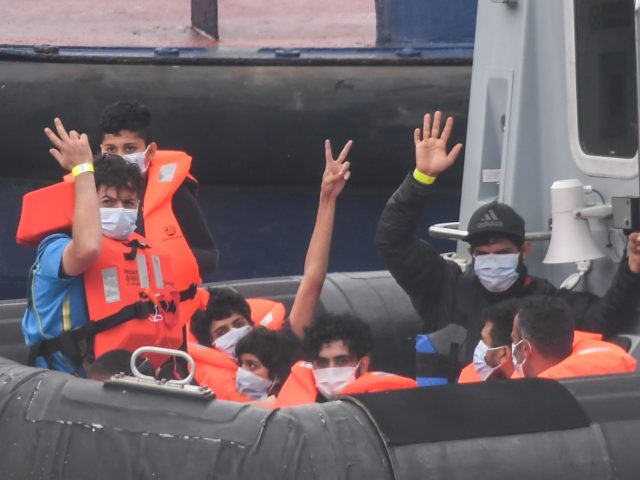 DOVER, ENGLAND - AUGUST 12: Migrants gesture as they arrive in port aboard a Border Force vessel after being intercepted while crossing the English Channel from France in small boats on August 12, 2020 in Dover, England. Favourable weather conditions in recent weeks have led to a rise in people …