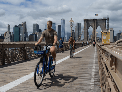 People bike over the Brooklyn Bridge from Manhattan in New York City on August 19, 2021. - President Joe Biden's administration announced steps on Thursday to allow US states to continue expanded unemployment benefits as the country grapples with a surge in the Delta variant of Covid-19, even as data …