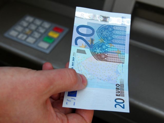 A man poses for the photographer with a twenty Euro note after withdrawing money from an a