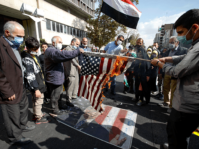 Iranian protesters step on a poster of President Joe Biden as they set a US flag on fire d