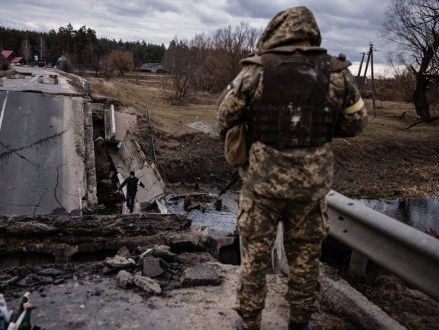 TOPSHOT - An Ukrainian serviceman looks at a civilian crossing a blown up bridge in a vill