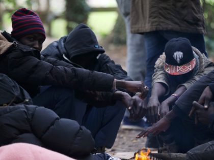 Sudanese migrants wait around a fire in a forest where they sleep in Ouistreham, near Caen
