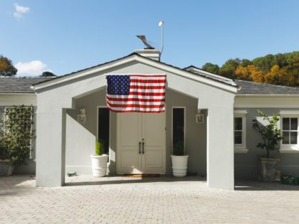 House decorated with american flag with landscape and blue sky with clouds in background