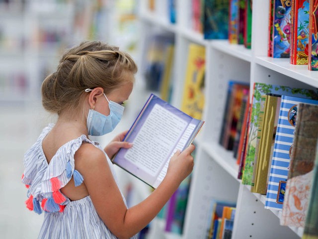 Girl in mask reading at a library. ( Irina Tiumentseva/iStock/Getty Images Plus)