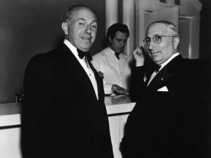 American film executives Jack L Warner (left, 1892 - 1978) and Louis B Mayer (1885 - 1957), both dressed in tuxedos, standing together at a bar, circa 1940.