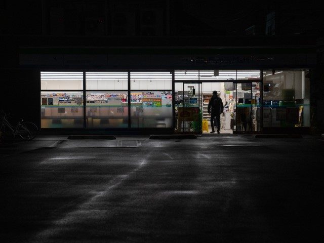 TOKYO, JAPAN - MARCH 22: A man enters a convenience store that has turned off its exterior lighting to conserve energy on March 22, 2022 in Tokyo, Japan. The energy usage reduction comes after a large earthquake last week affected power stations supplying the Tokyo area, forcing the government to …