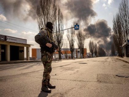 A Ukrainien serviceman stands guard near a burning warehouse hit by a Russian shell in the