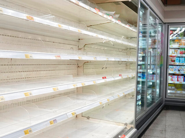 A woman wearing face mask looks at empty shelves as residents worry about a shortage of fo