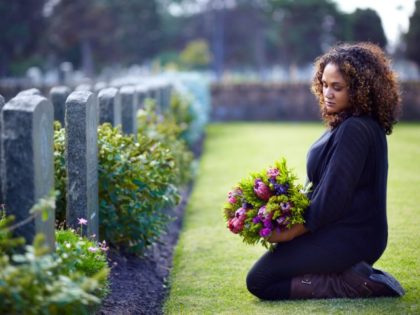 Woman kneels at loved one's grave.