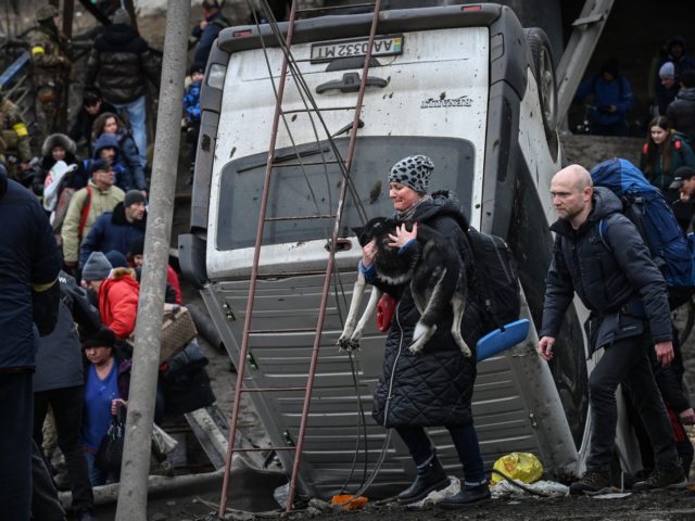 TOPSHOT - A woman carries a dog while people cross a destroyed bridge as they evacuate the city of Irpin, northwest of Kyiv, during heavy shelling and bombing on March 5, 2022, 10 days after Russia launched a military in vasion on Ukraine. (Photo by Aris Messinis / AFP) (Photo …