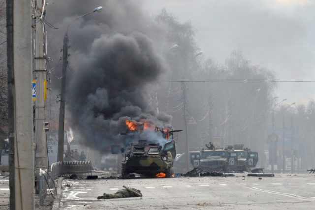 A Russian armoured personnel carrier burns next to an unidentified soldier's body in Khark