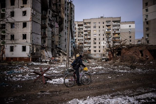 A man rides his bicycle on March 4, 2022 in front of residential buildings damaged in shel