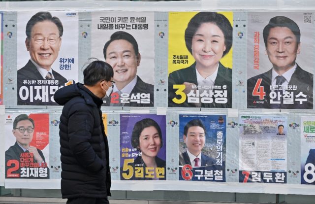 A man walks past posters of South Korea's presidential candidates (top row) in Seoul on Ma