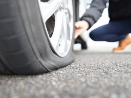 A man crouches on the road to inspect a flat tire.