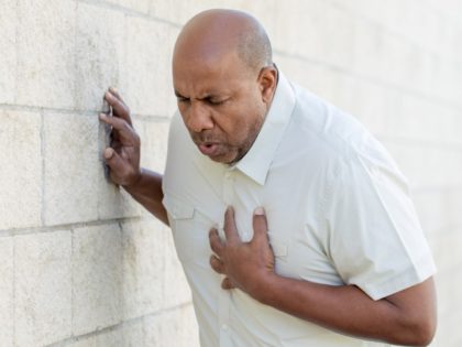 A man having chest pains leans against a cinderblock wall.