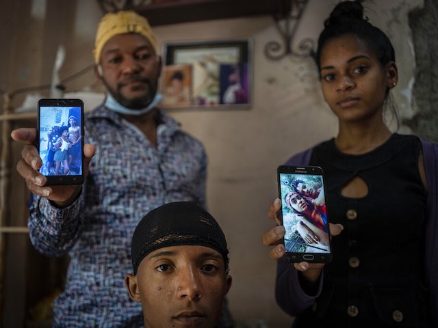 Odlanier Santiago Rodríguez, center, who was accused of participating in the recent anti-government protests and who was released after 22 days in prison, poses with his uncle Emilio Roman, left, and his daughter-in-law María Carla Milán Ramos, as they show photos of Roman´s three children who are still in prison accused of participating in the recent protets against the government, in the La Guinera neighborhood of Havana, Cuba, Wednesday, Jan. 19, 2022. Six months after surprising protests against the Cuban government, more than 50 protesters who have been charged with sedition are headed to trial and could face sentences of up to 30 years in prison. (AP Photo/Ramon Espinosa)