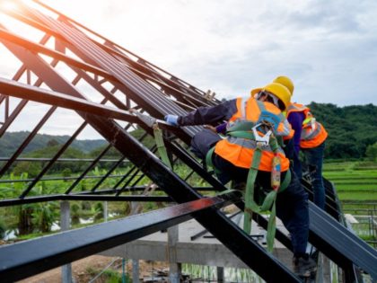 Construction worker wearing safety harness using secondary safety device connecting into 15 mm static rope using as fall restraint shingle on top of the new roof.