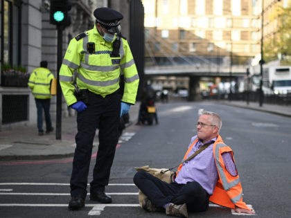 A police officer stands next to a climate activist from the group Insulate Britain whose hands are glued to the ground as he blocks a street in central London calling for the UK government to fund the insulation of Britain's homes on October 25, 2021. - Britain is eager to …