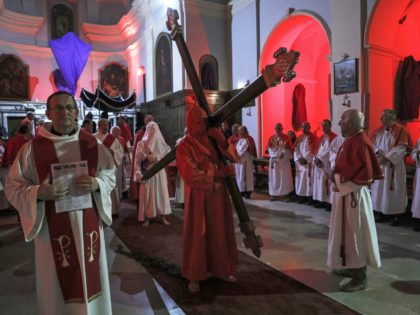 Catholic faithfuls follow as the "grand penitent" walks holding the wood cross in the Sainte Marie church before the start of the "Catenacciu" night procession on Good Friday in Sartene, on the French Mediterranean island of Corsica, late on April 15, 2022. (Photo by Pascal POCHARD-CASABIANCA / AFP) (Photo by …