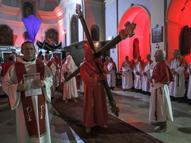 Catholic faithfuls follow as the "grand penitent" walks holding the wood cross in the Sainte Marie church before the start of the "Catenacciu" night procession on Good Friday in Sartene, on the French Mediterranean island of Corsica, late on April 15, 2022. (Photo by Pascal POCHARD-CASABIANCA / AFP) (Photo by …