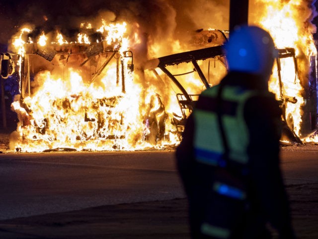An anti-riot police officer stands next to a city bus burning in Malmo late April 16, 2022