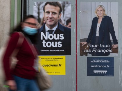 A woman passes by electoral campaign posters of French President and La Republique en Marche (LREM) party candidate for re-election Emmanuel Macron (L) and French far-right party Rassemblement National (RN) presidential candidate Marine Le Pen in Savenay, western France on April 19, 2022. - Emmanuel Macron won 27.85 percent of …