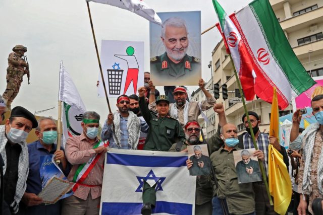 Iranians prepare to set an Israeli flag on fire next to a picture of late Iranian general