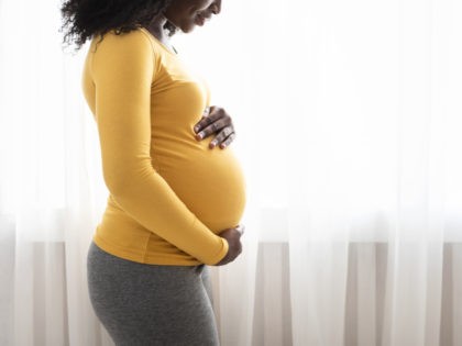 Beautiful pregnant black woman hugging her tummy, enjoying her pregnancy, free space. Side