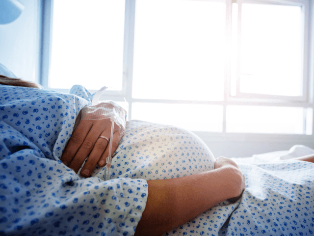 Close-up of a pregnant woman's belly in the hospital bed with catheter in hand