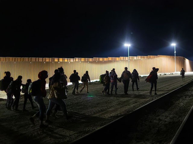 YUMA, ARIZONA - DECEMBER 07: Immigrants walk along the U.S. border wall after crossing from Mexico through a nearby gap in the fence on December 07, 2021 in Yuma, Arizona. U.S. Border Patrol agents said that the detention facility in Yuma was full and they had stopped taking in more immigrants for the day. Immigration officials were overwhelmed processing thousands of new arrivals, with many families trying to reach U.S. soil before the court-ordered re-implementation of the Trump-era Remain in Mexico policy. The policy requires asylum seekers to stay in Mexico for the duration of their U.S. immigration court process. (Photo by John Moore/Getty Images)