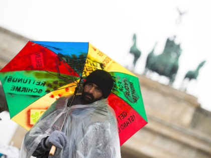 A refugee shelters from the rain with an umbrella during a "camp-in" hunger strike of refugees in which they also refuse drinking water in front of the Brandenburg Gate in Berlin on October 15, 2013. Around 30 refugees demonstrate since almost a week in front of the German capital's landmark …