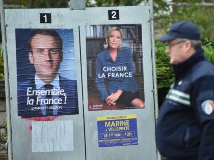 Police officers walk past campaign posters of French presidential election candidate for the En Marche ! movement Emmanuel Macron (L) and French presidential election candidate for the far-right Front National (FN - National Front) party Marine Le Pen in Le Touquet, on May 7, 2017, during the second round of …