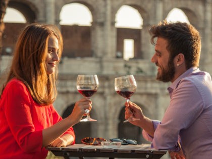 Romantic couple drinking glass of red wine sitting at restaurant table in front of colosse
