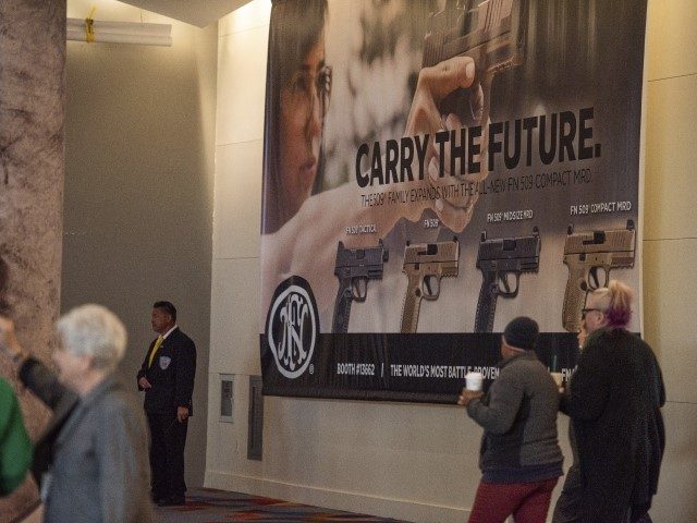 This photo taken Monday, Jan. 20, 2020, shows people walking by a sign advertising firearms from gunmaker FN Herstal, with operations in Belgium and the United States, on display at SHOT Show, the annual trade show for the gun industry in Las Vegas. The show is sponsored by the National …