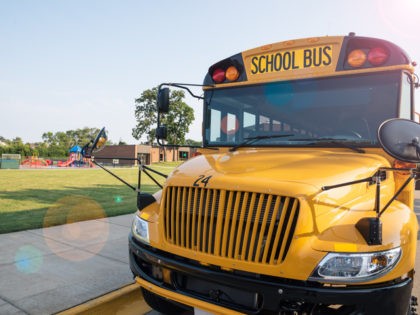 Yellow school bus parked in front of a school playground. (DavidPrahl/Getty Images Stock)