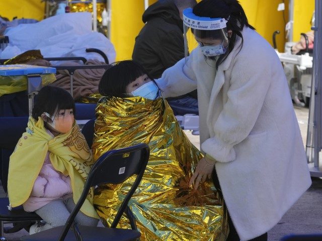 A woman with children wearing face masks wait at a temporary makeshift treatment area outs