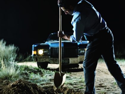 Young man digging hole in front of car in desert at night, side view