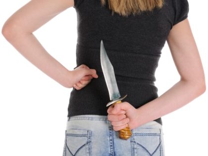 A young woman holds a knife behind her back.