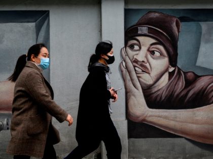 People wearing face masks walk past a mural along a street in Wuhan, China's central Hubei province on April 2, 2020. - Wuhan, the epicentre of the coronavirus pandemic, is very slowly re-emerging from more than two months of demoralising lockdown. But endless rows of plastic yellow or blue barriers …