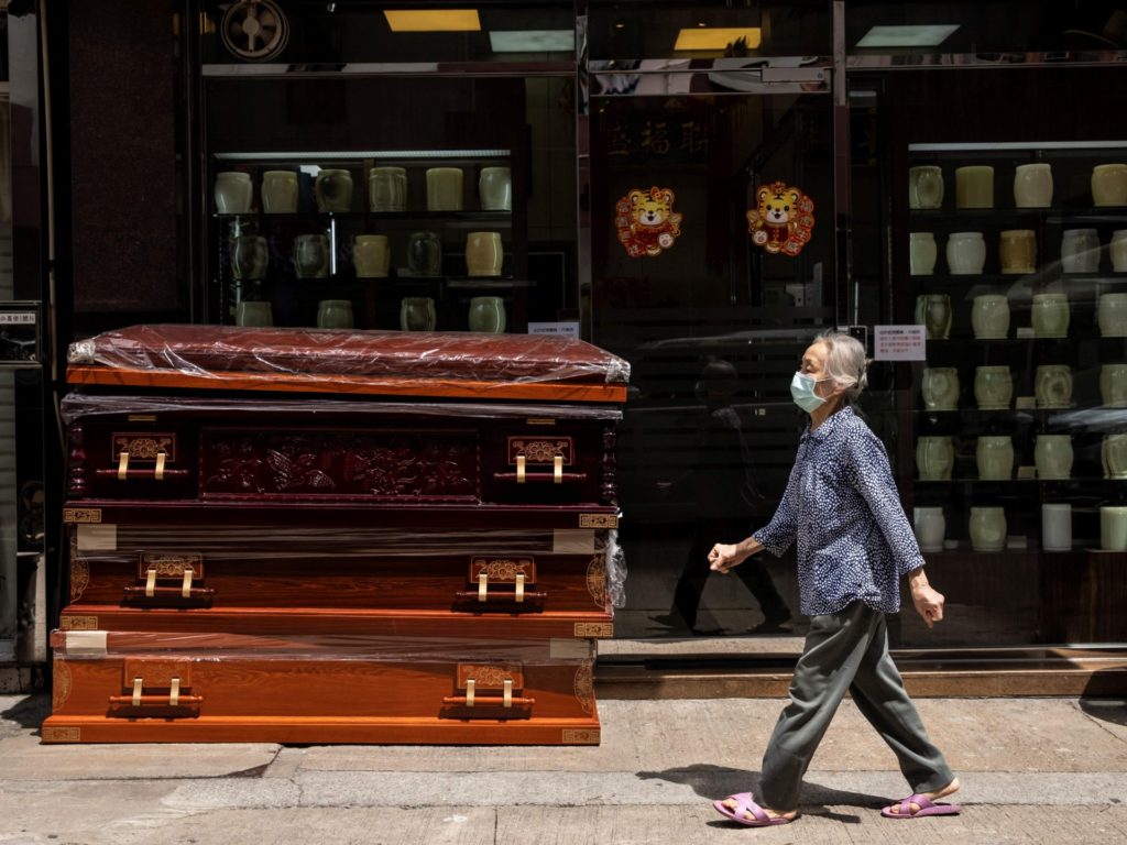 A woman walks past empty coffins (L) stacked up outside a funeral services shop in the Kowloon district of Hong Kong on March 17, 2022. - A funeral industry representative on March 16 told local media the soaring death toll due to Covid-19 had seen a crunch in the city's coffins supply, with only 300 remaining and expected to be gone by the weekend. (Photo by ISAAC LAWRENCE / AFP) (Photo by ISAAC LAWRENCE/AFP via Getty Images)